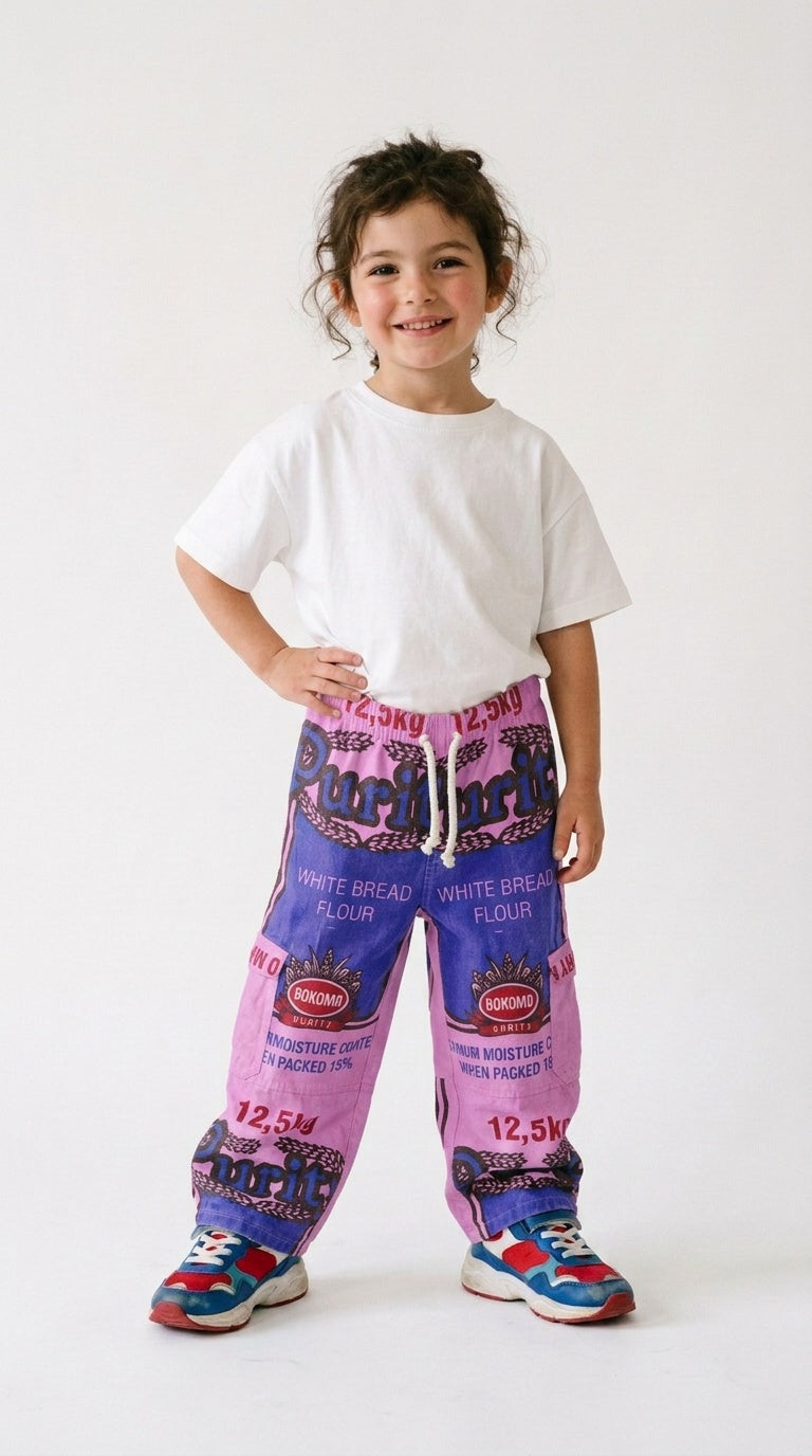 Smiling toddler in a white tee and colourful sneakers wearing kids’ Purity Bokomo flour bag pants